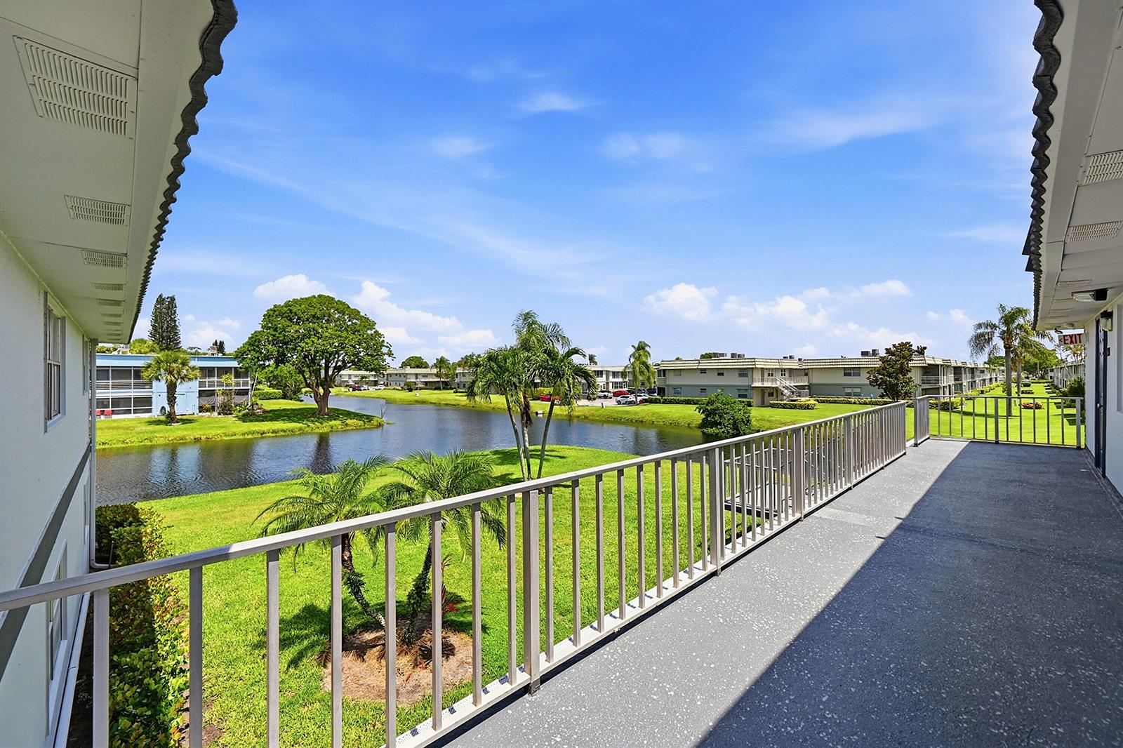An elevated outdoor balcony overlooks a grassy lawn, a small pond, and surrounding apartment buildings — 383 Saxony Lane # H, Delray Beach FL 33446, DELRAY BEACH, FL