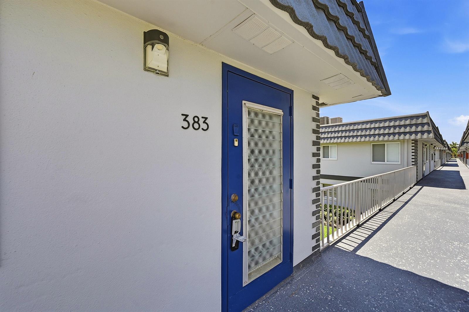 A blue front door with a textured glass panel is numbered 383 on an exterior walkway — 383 Saxony Lane # H, Delray Beach FL 33446, DELRAY BEACH, FL