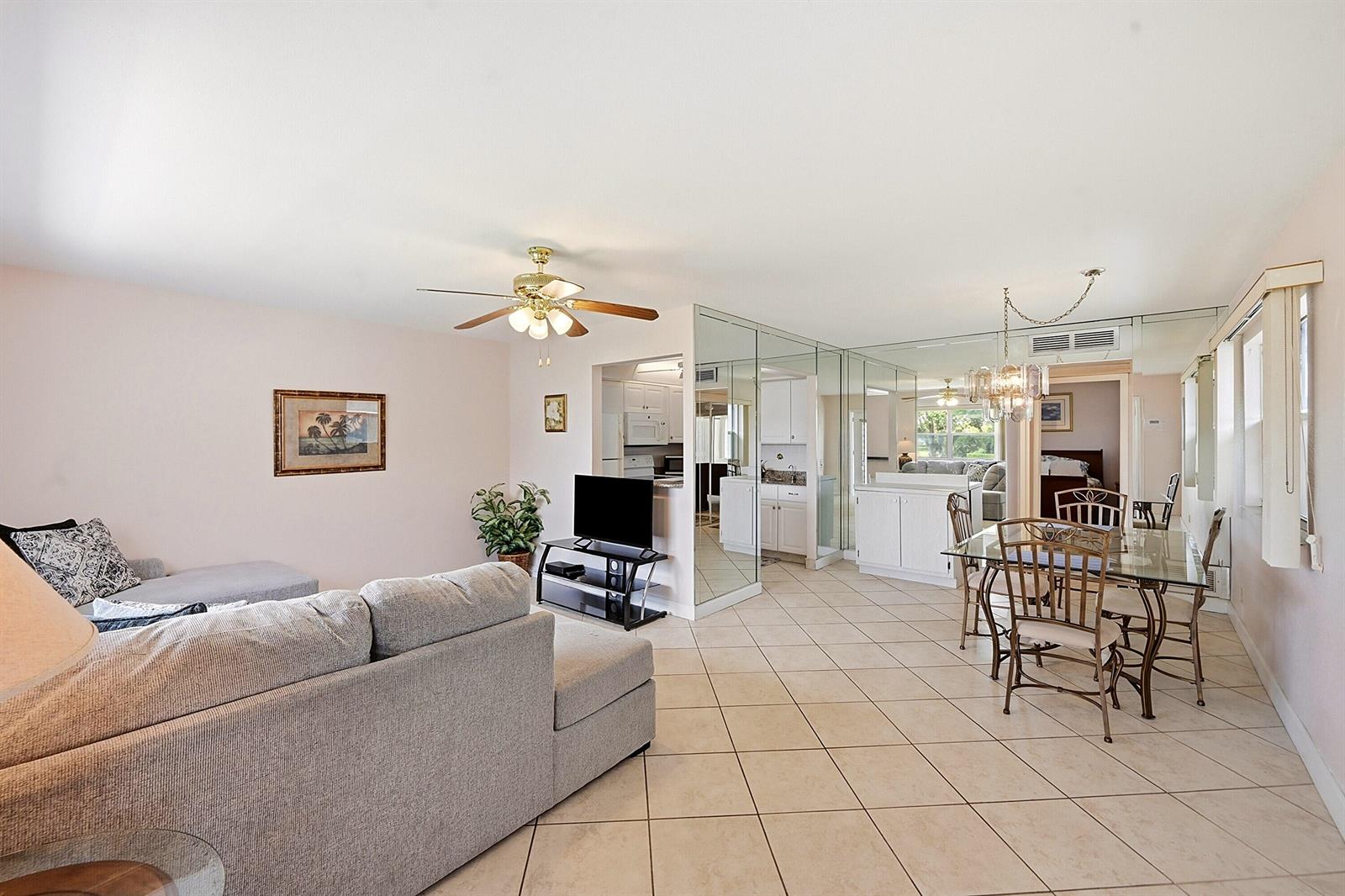 A living and dining area with tile floors, a mirrored wall, and a ceiling fan — 383 Saxony Lane # H, Delray Beach FL 33446, DELRAY BEACH, FL