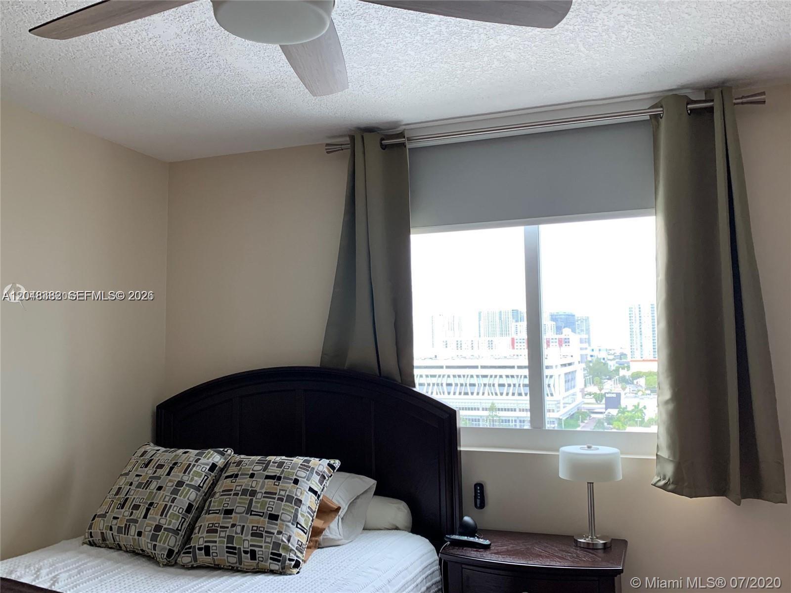 A bedroom features a dark wood headboard, patterned pillows, a nightstand, and a city view — 275 NE 18th St # 1109, Miami FL 33132, MIAMI, FL