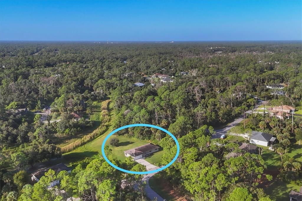 An aerial view shows a single-story house surrounded by dense trees and a grassy yard — 2415 NOWATNEY AVENUE, NORTH PORT, FL