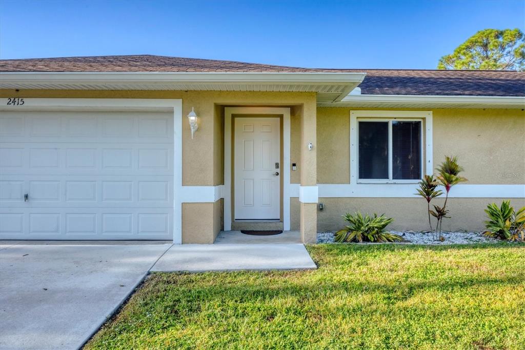 The exterior of a single-story house features a garage, a front door, and landscaping — 2415 NOWATNEY AVENUE, NORTH PORT, FL