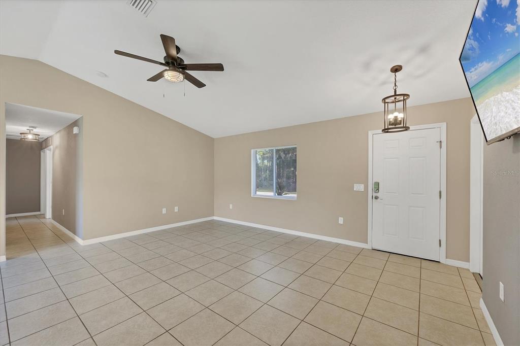 A living room with beige walls, tile flooring, a ceiling fan, and a front door — 2415 NOWATNEY AVENUE, NORTH PORT, FL