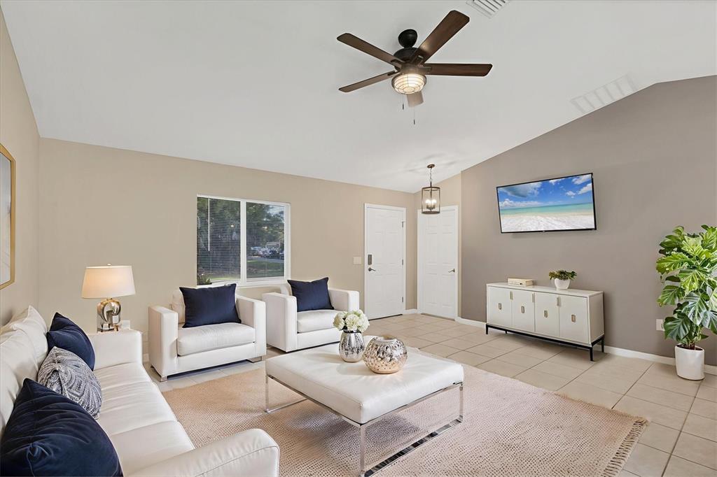 A living room features white furniture, a ceiling fan, and a wall-mounted television — 2415 NOWATNEY AVENUE, NORTH PORT, FL