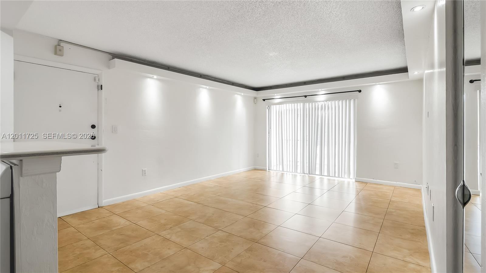 An empty room features white walls, tan tile flooring, recessed lighting, and sliding glass doors — 7200 Fairway Dr # H12, Miami Lakes FL 33014, MIAMI LAKES, FL