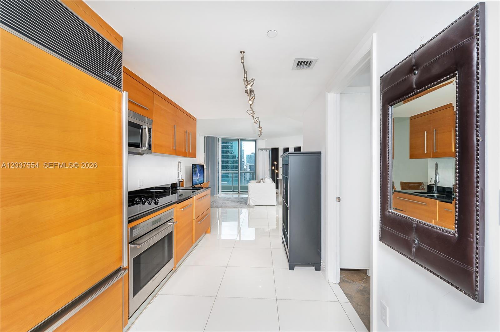 A galley kitchen features light wood cabinets, stainless steel appliances, and white tile flooring — 475 Brickell Ave # 2908, Miami FL 33131, MIAMI, FL