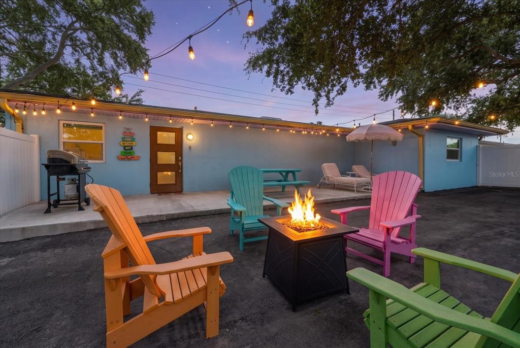A backyard patio features a fire pit, colorful Adirondack chairs, string lights, and a grill — 2050 W BAY DRIVE, LARGO, FL