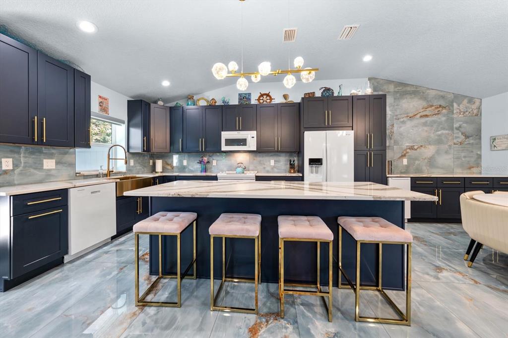 A kitchen features dark blue cabinets, a central island with pink stools, and marble flooring — 2050 W BAY DRIVE, LARGO, FL