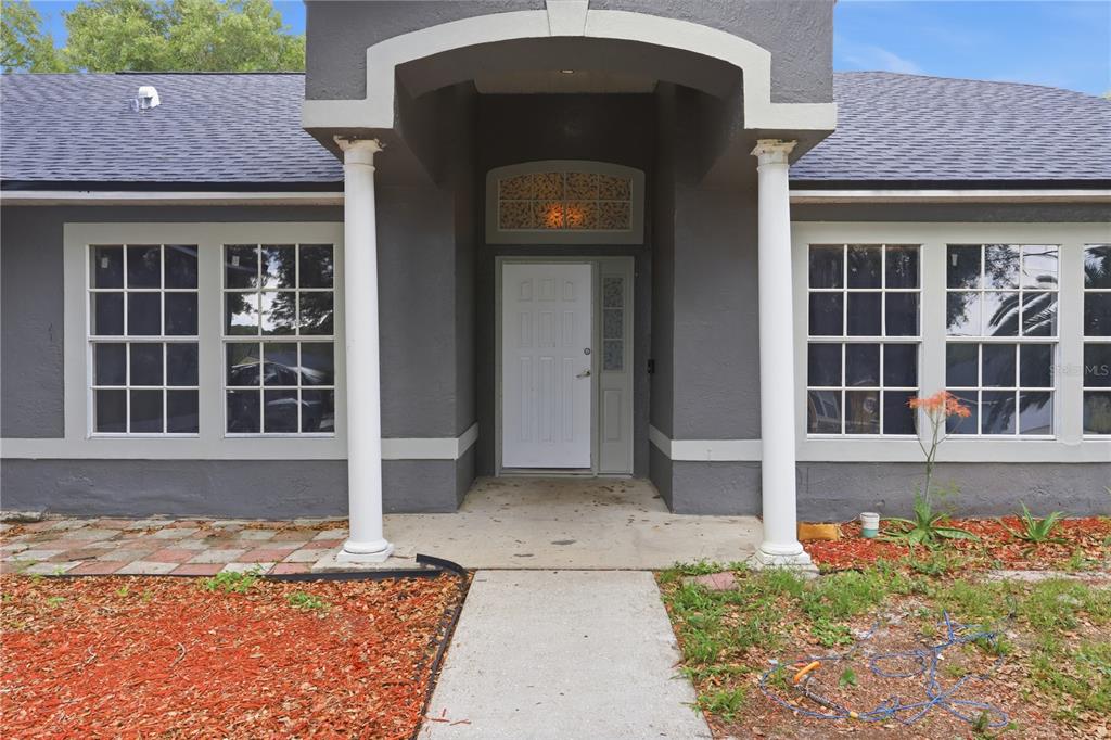 The exterior of a gray house features a white front door, columns, and a walkway — 725 W 9TH STREET, DELTONA, FL
