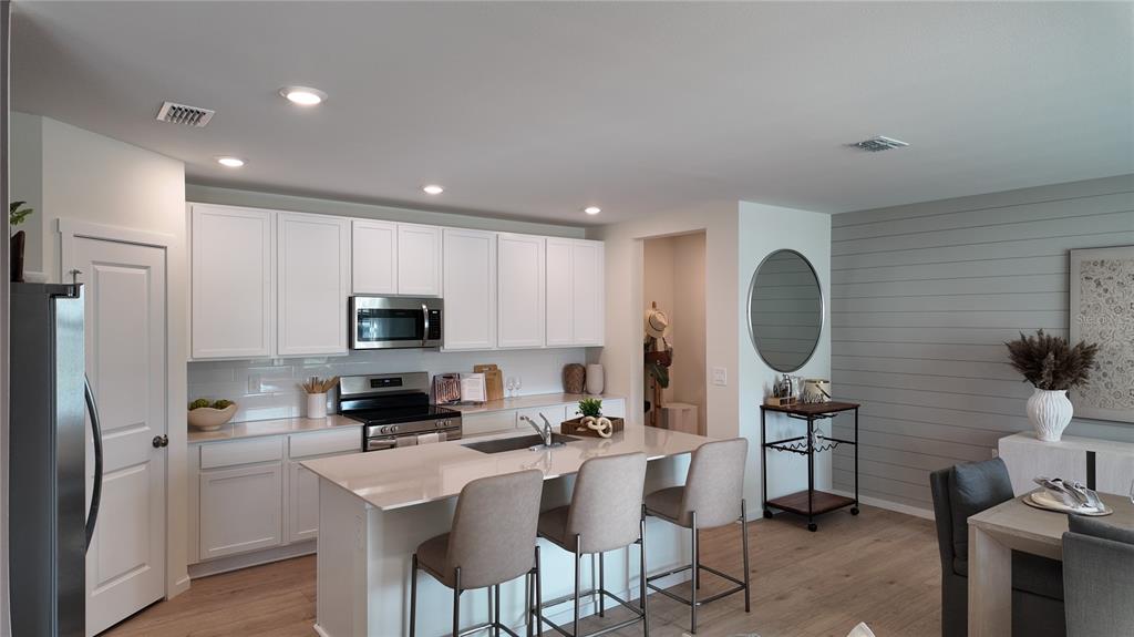 A modern kitchen features white cabinets, a central island with bar stools, and light flooring — 4443 ELLIOTS ASTOR BOULEVARD, ST CLOUD, FL