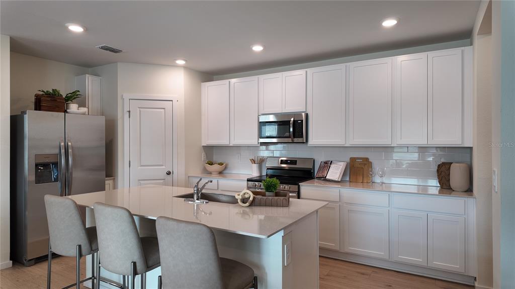 A modern kitchen features white cabinets, stainless steel appliances, a quartz island, and bar seating — 4443 ELLIOTS ASTOR BOULEVARD, ST CLOUD, FL