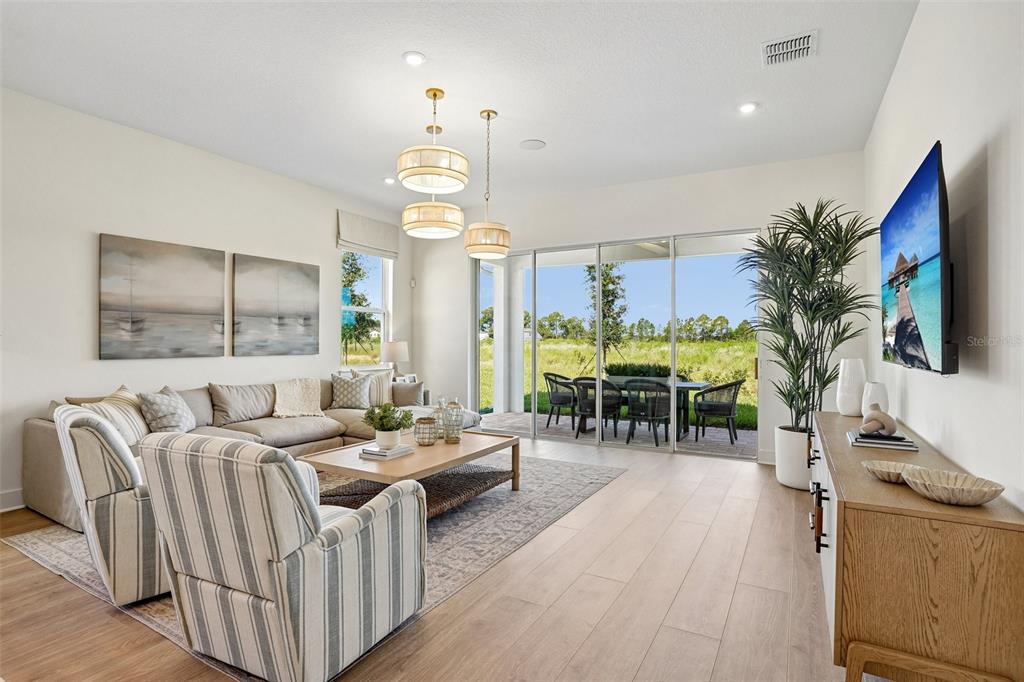 A living room features a sectional sofa, striped armchairs, and sliding glass doors to a patio — 17406 HONEYBELL TANGELO COURT, WINTER GARDEN, FL