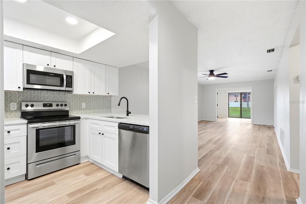 A kitchen with white cabinets and stainless steel appliances opens into a living area — 13250 RIDGE ROAD UNIT 9-1, LARGO, FL