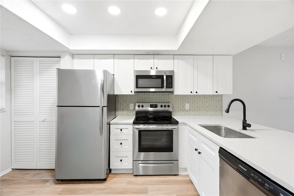A kitchen features white cabinets, stainless steel appliances, a herringbone backsplash, and light wood flooring — 13250 RIDGE ROAD UNIT 9-1, LARGO, FL