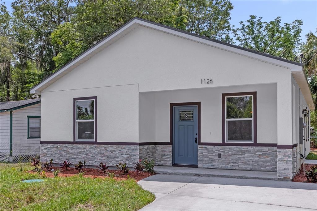 A single-story house with white stucco walls, stone veneer accents, and a blue front door — 1126 S THOMPSON AVENUE, DELAND, FL