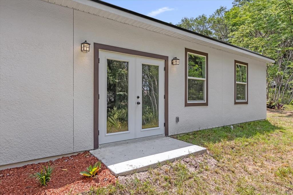 A white stucco house exterior features a set of French doors and two windows — 1126 S THOMPSON AVENUE, DELAND, FL