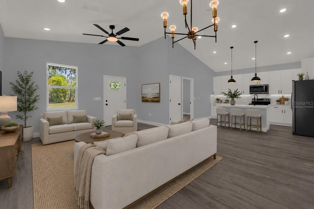 A bright, open-concept living room and kitchen featuring vaulted ceilings, light gray walls, and flooring — 1126 S THOMPSON AVENUE, DELAND, FL
