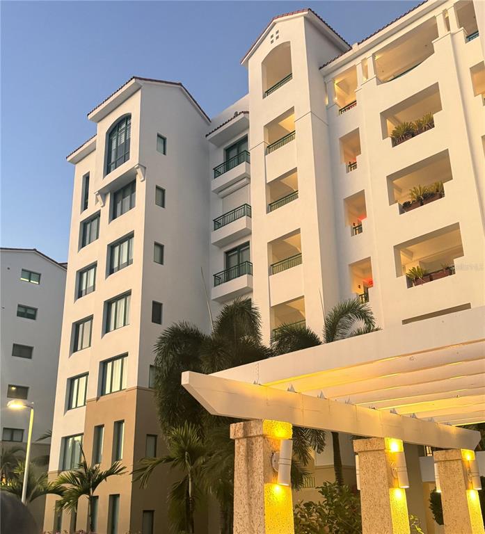 A low-angle exterior view of a multi-story white apartment building with balconies and palm trees — Ocean Sixteen 9000 RIO MAR BLVD UNIT 321, RIO GRANDE, PR