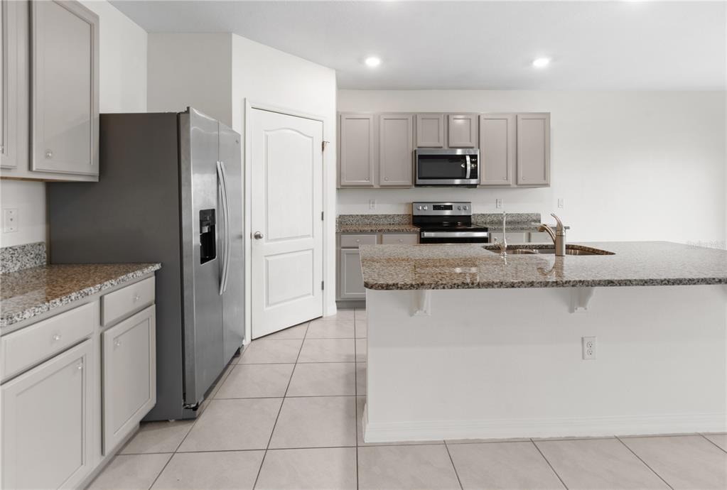 An open-concept kitchen and living area with gray cabinets, granite countertops, and tile flooring — 2651 GRANDBURY GROVE ROAD, LAKELAND, FL