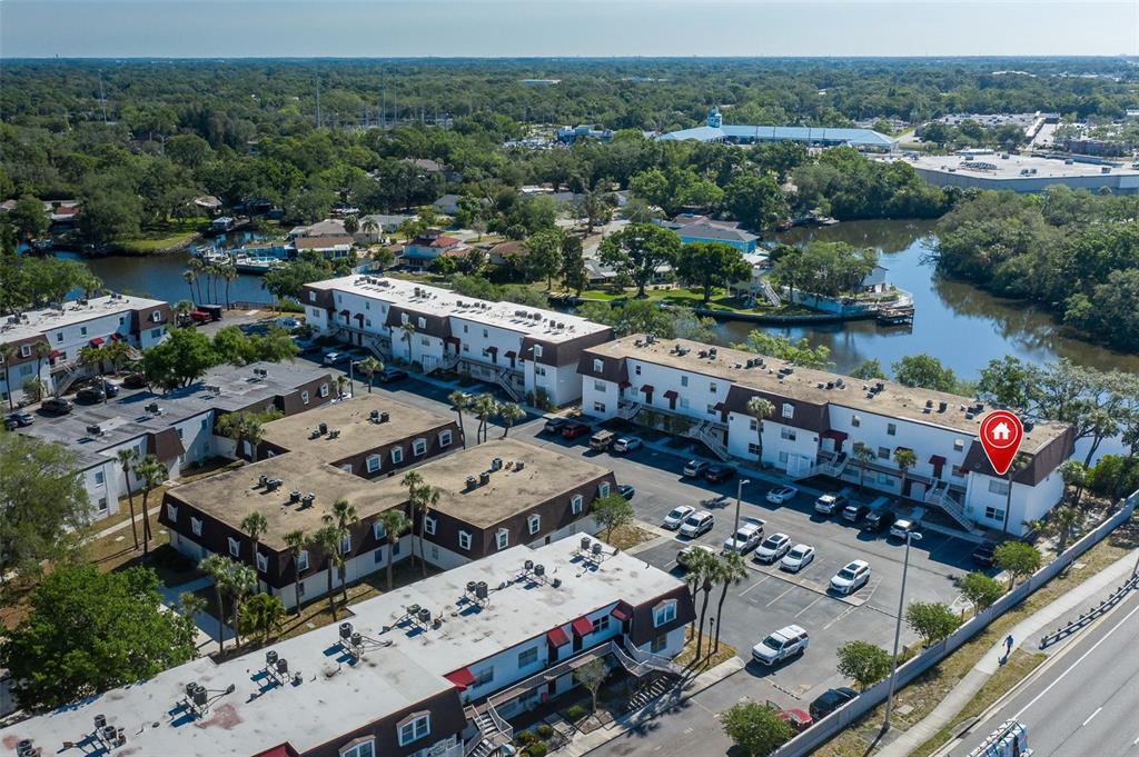 An aerial view shows multi-story apartment buildings with flat roofs and parking lots near a waterway — 9001 TUDOR DRIVE UNIT H210, TAMPA, FL