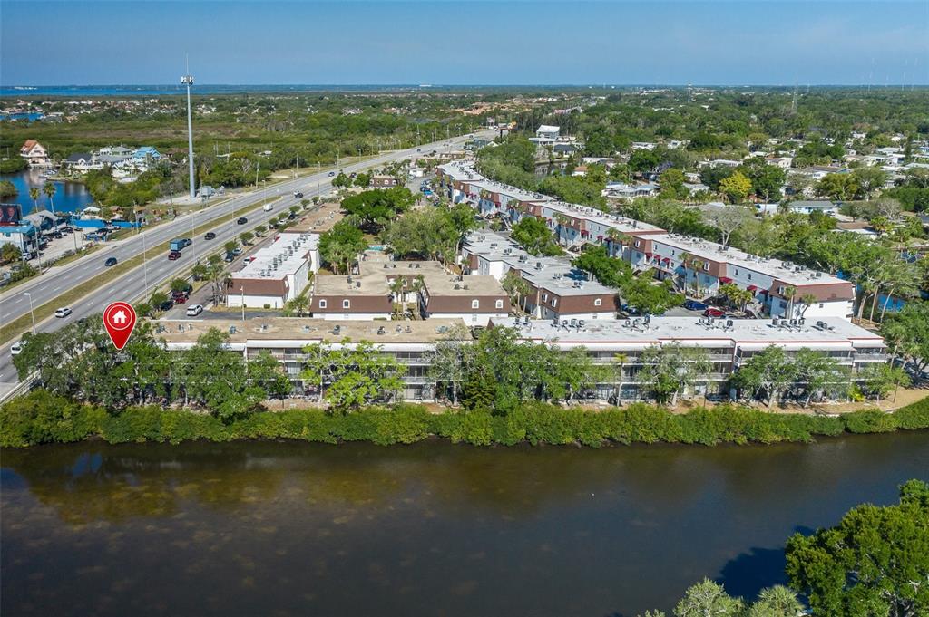An aerial view shows a multi-story apartment complex situated along a waterfront with a highway — 9001 TUDOR DRIVE UNIT H210, TAMPA, FL