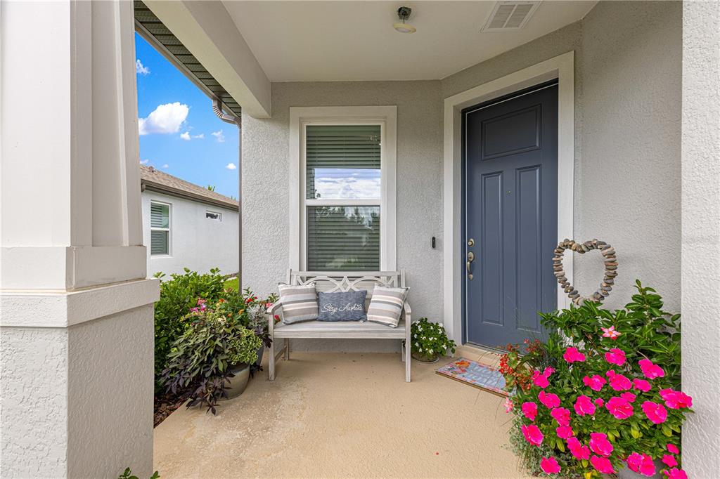 A covered front porch features a blue door, a wooden bench, and potted flowering plants — 8776 SW 58TH STREET ROAD, OCALA, FL