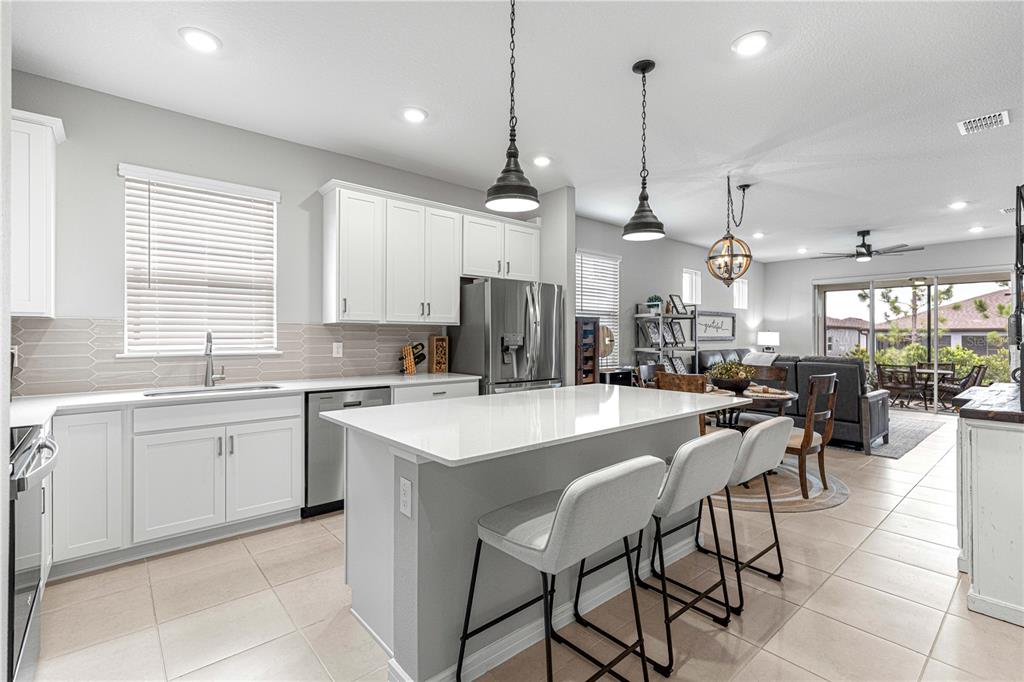 A modern kitchen features white cabinets, a quartz-topped island with bar seating, and tile flooring — 8776 SW 58TH STREET ROAD, OCALA, FL