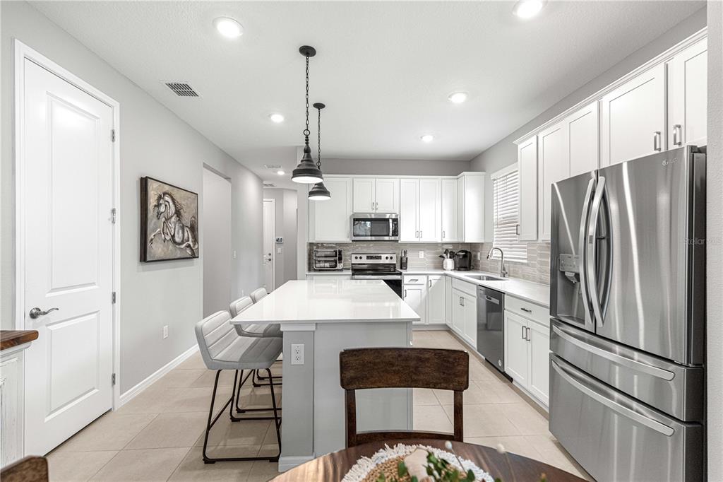 A modern kitchen features white cabinetry, a large island with bar seating, and stainless appliances — 8776 SW 58TH STREET ROAD, OCALA, FL