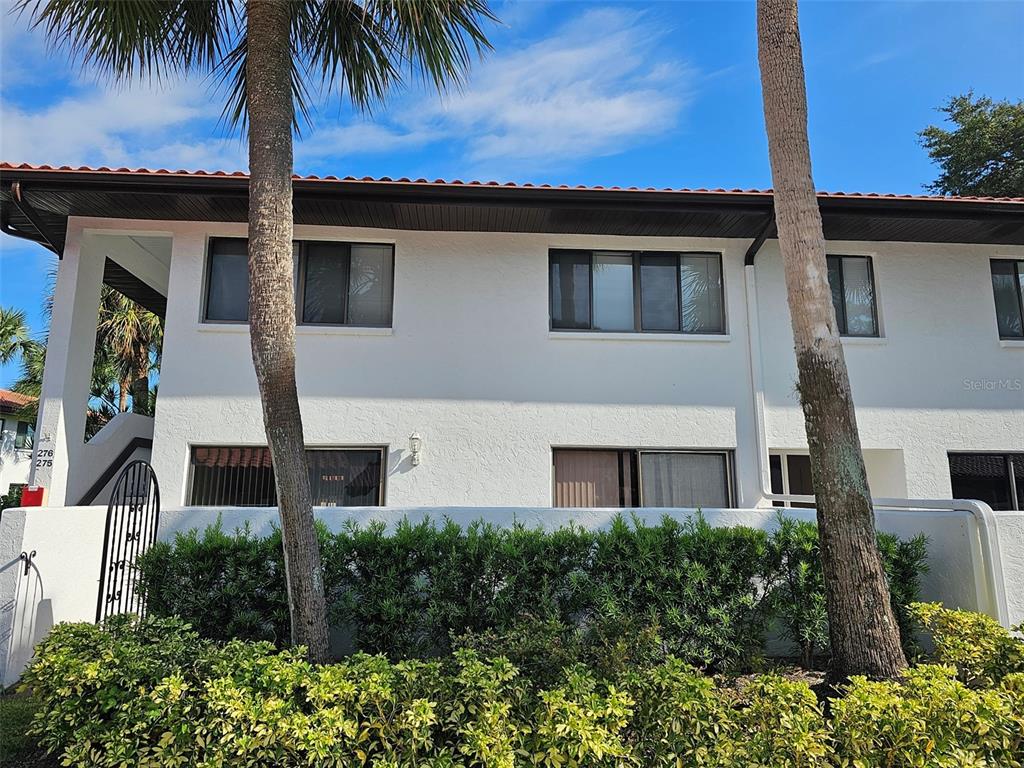 A two-story white stucco building features a tiled roof, palm trees, and a hedge — 3500 EL CONQUISTADOR PARKWAY UNIT 275, BRADENTON, FL