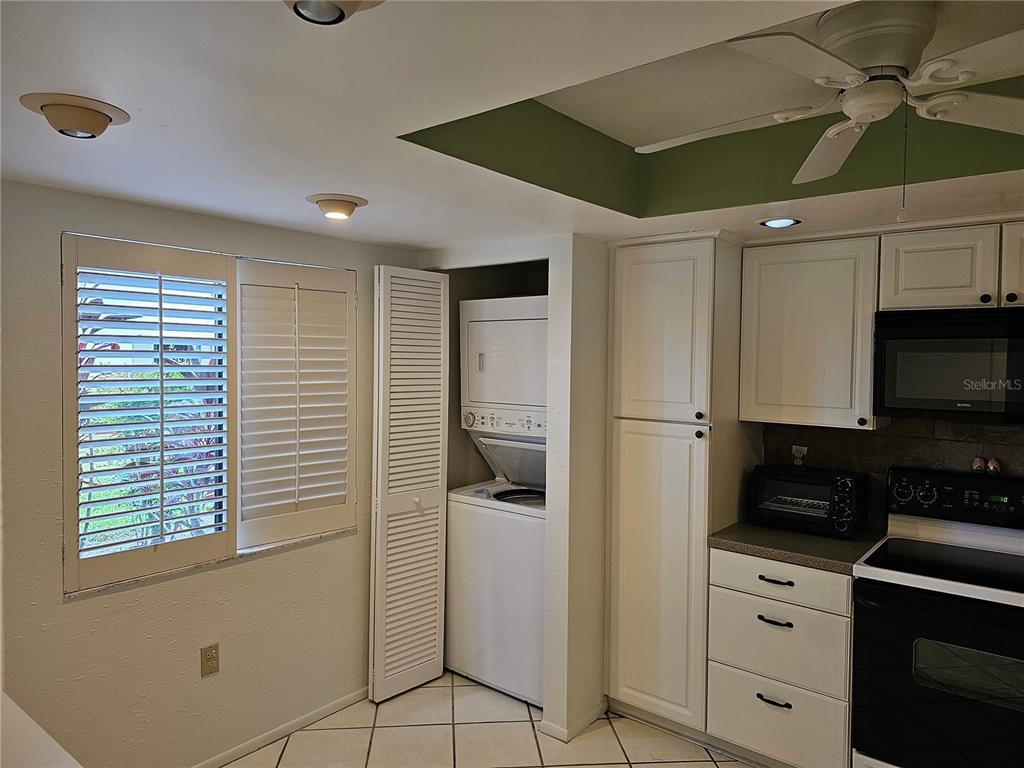 A kitchen features white cabinets, a stacked washer and dryer, and a window with shutters — 3500 EL CONQUISTADOR PARKWAY UNIT 275, BRADENTON, FL