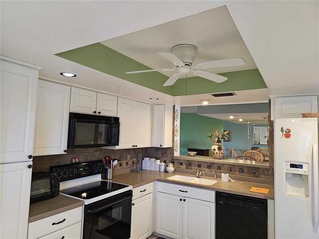 A kitchen features white cabinetry, dark countertops, a green tray ceiling, and a ceiling fan — 3500 EL CONQUISTADOR PARKWAY UNIT 275, BRADENTON, FL