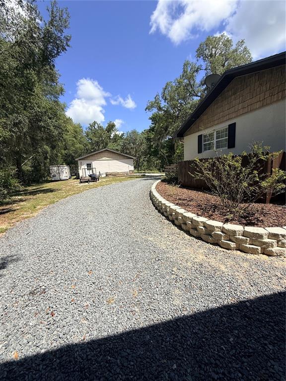 A gravel driveway leads toward a detached garage next to a house with a retaining wall — 25962 WHIPPERWILL STREET, BROOKSVILLE, FL