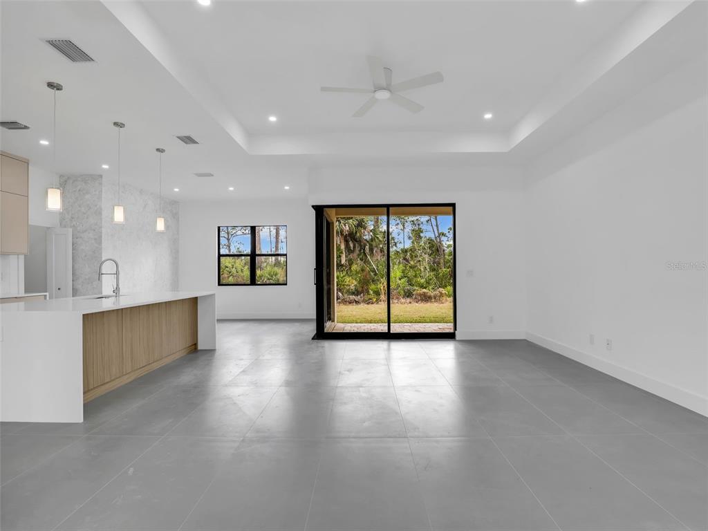 A modern open-concept kitchen and living area with white walls, gray tile flooring, and sliding doors — 11161 CARNEGIE AVENUE, ENGLEWOOD, FL