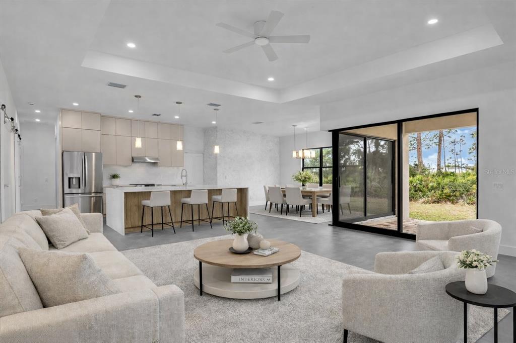 An open-concept living room and kitchen with light-toned cabinetry, a tray ceiling, and sliding doors — 11161 CARNEGIE AVENUE, ENGLEWOOD, FL