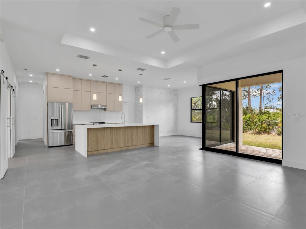 A modern kitchen features light wood cabinets, a white island, and large sliding glass doors — 11161 CARNEGIE AVENUE, ENGLEWOOD, FL