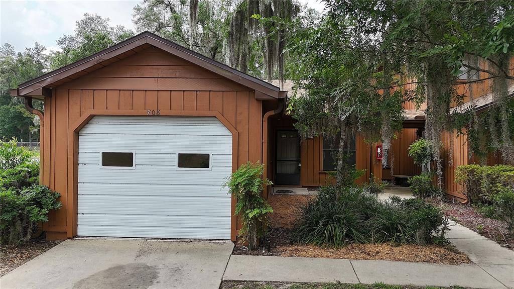A brown house with a white garage door and a covered entryway surrounded by trees — 2701 NE 10TH STREET UNIT 708, OCALA, FL