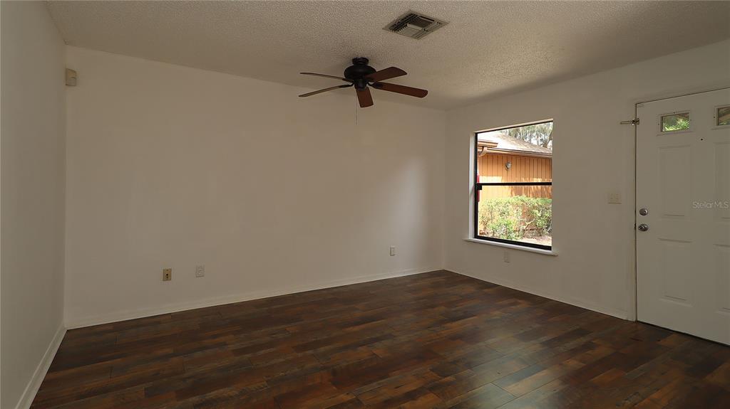 An empty room features dark wood-look flooring, a ceiling fan, and a white entry door — 2701 NE 10TH STREET UNIT 708, OCALA, FL