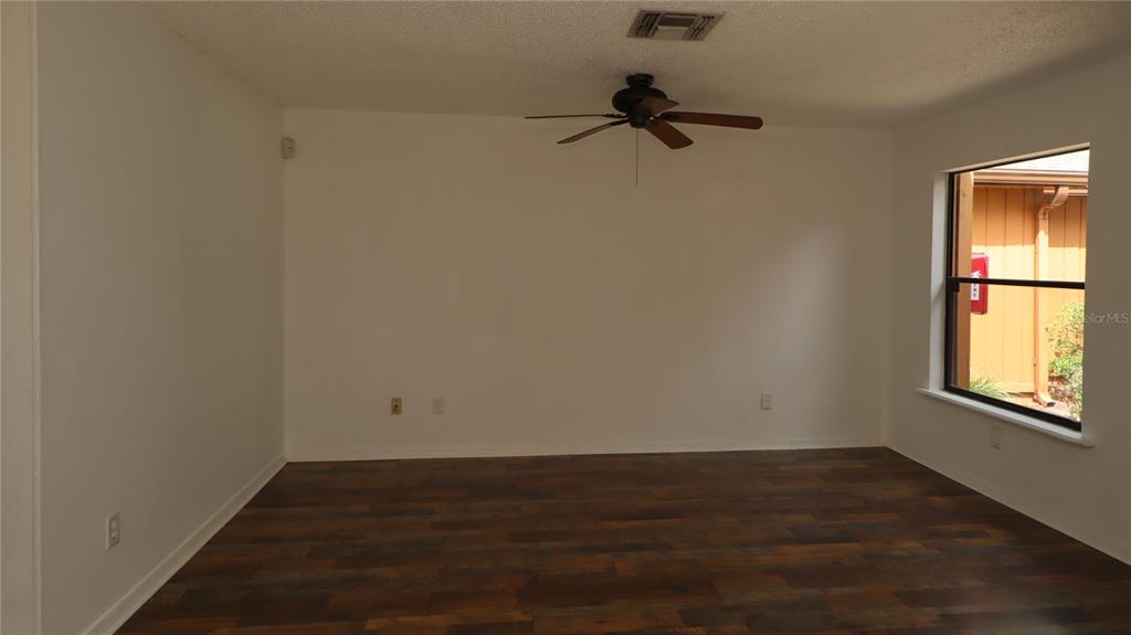 An empty room features white walls, dark wood-look flooring, a ceiling fan, and one window — 2701 NE 10TH STREET UNIT 708, OCALA, FL