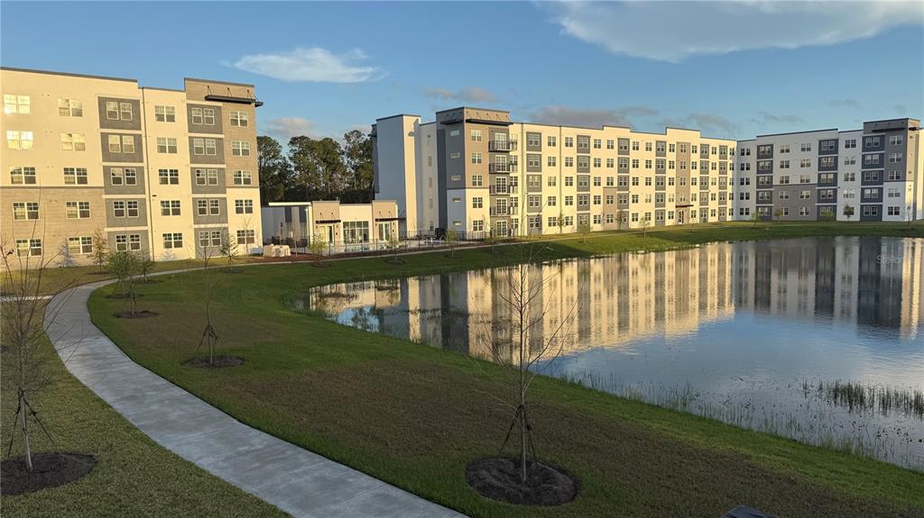 A multi-story apartment complex sits beside a pond with a paved walking path in front — 5579 MILLENIA PARK BOULEVARD UNIT 201, ORLANDO, FL