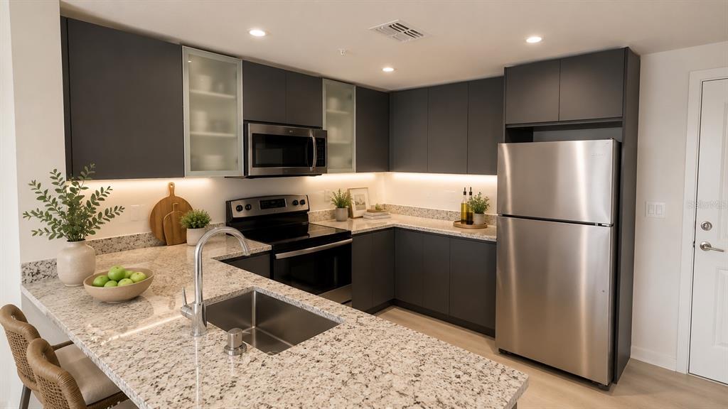 A modern kitchen features dark gray cabinetry, granite countertops, stainless steel appliances, and a peninsula — 5579 MILLENIA PARK BOULEVARD UNIT 201, ORLANDO, FL