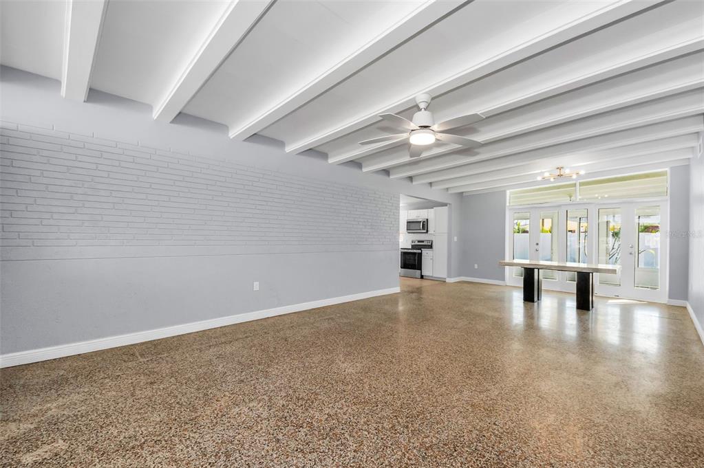 A spacious room with a white beamed ceiling, gray brick wall, and polished concrete floors — 414 88TH AVENUE, ST PETE BEACH, FL