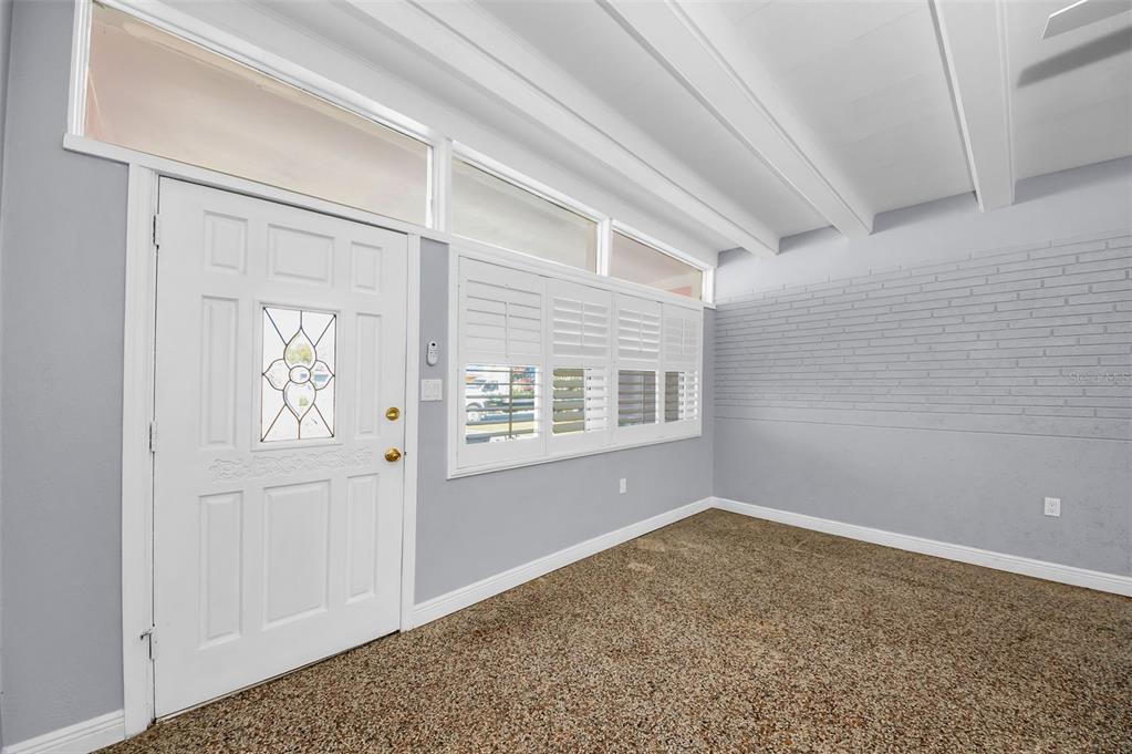 An entryway features a white front door, shuttered windows, a vaulted ceiling, and carpeted flooring — 414 88TH AVENUE, ST PETE BEACH, FL