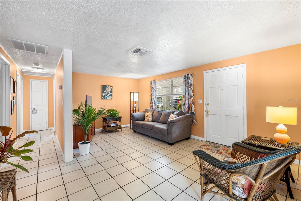 A living room features peach-colored walls, white tile flooring, a gray sofa, and a front door — 5638 146TH TERRACE N, CLEARWATER, FL