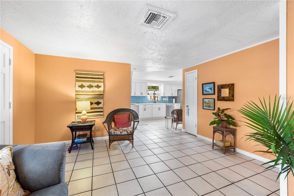 A living room with orange walls and tile flooring opens into a white kitchen — 5638 146TH TERRACE N, CLEARWATER, FL