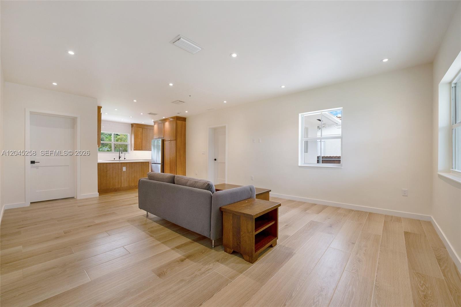 An open-concept living room features light wood-look flooring, a gray sofa, and an adjacent kitchen — 6356 SW 14th St, West Miami FL 33144, WEST MIAMI, FL