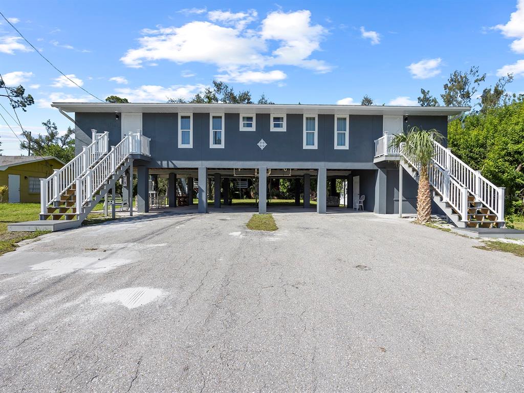 A two-story elevated gray building with two exterior staircases and a paved parking area underneath — 23019 SENECA AVENUE UNIT B, PORT CHARLOTTE, FL