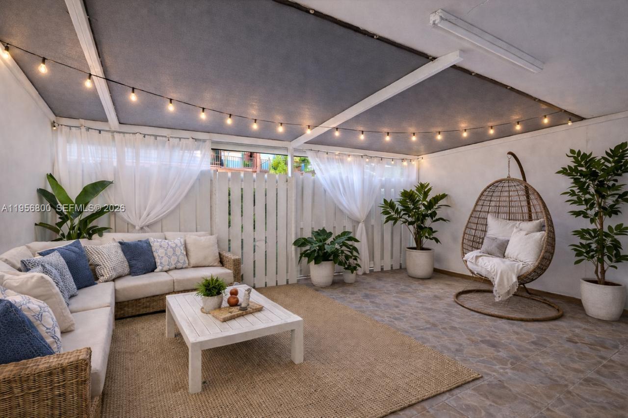 A covered outdoor patio features a wicker sofa, hanging chair, potted plants, and string lights — 850 SW 129th Pl # 103, Miami FL 33184, MIAMI, FL