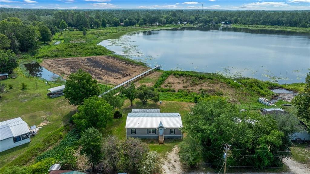 An aerial view shows a house with a metal roof near a lake and dock — 8581 NE 147TH COURT, SILVER SPRINGS, FL