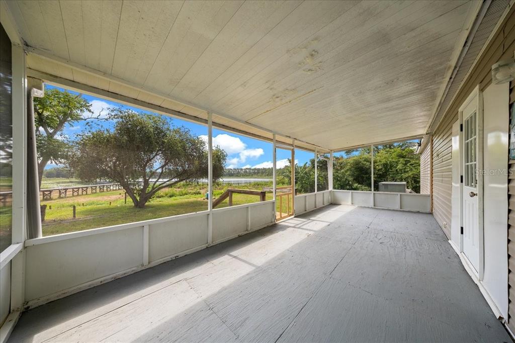 A screened-in porch with a gray floor overlooks a grassy yard and a lake — 8581 NE 147TH COURT, SILVER SPRINGS, FL
