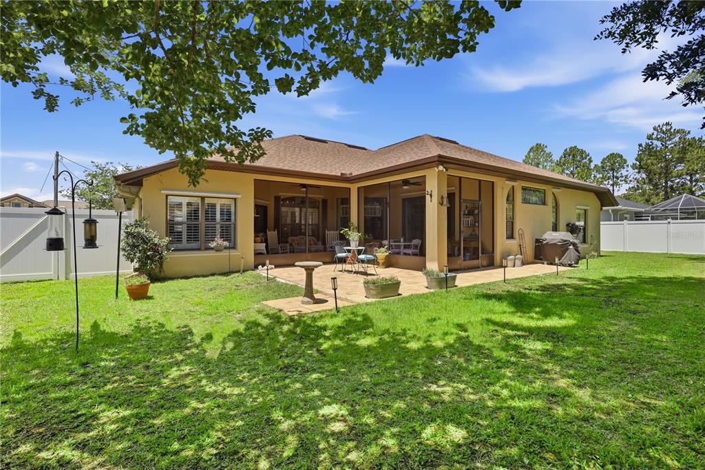 The backyard features a tan house with a screened-in patio and a paved stone area — 36 LANCASTER LANE, PALM COAST, FL